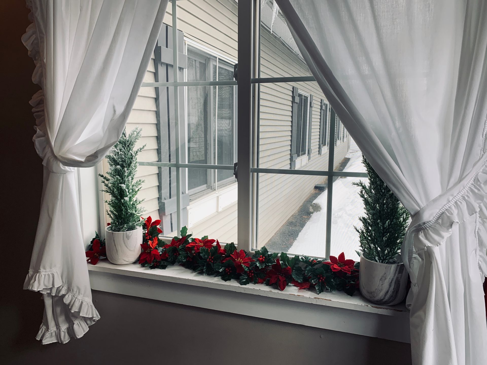 A window with white curtains and christmas decorations on the window sill.