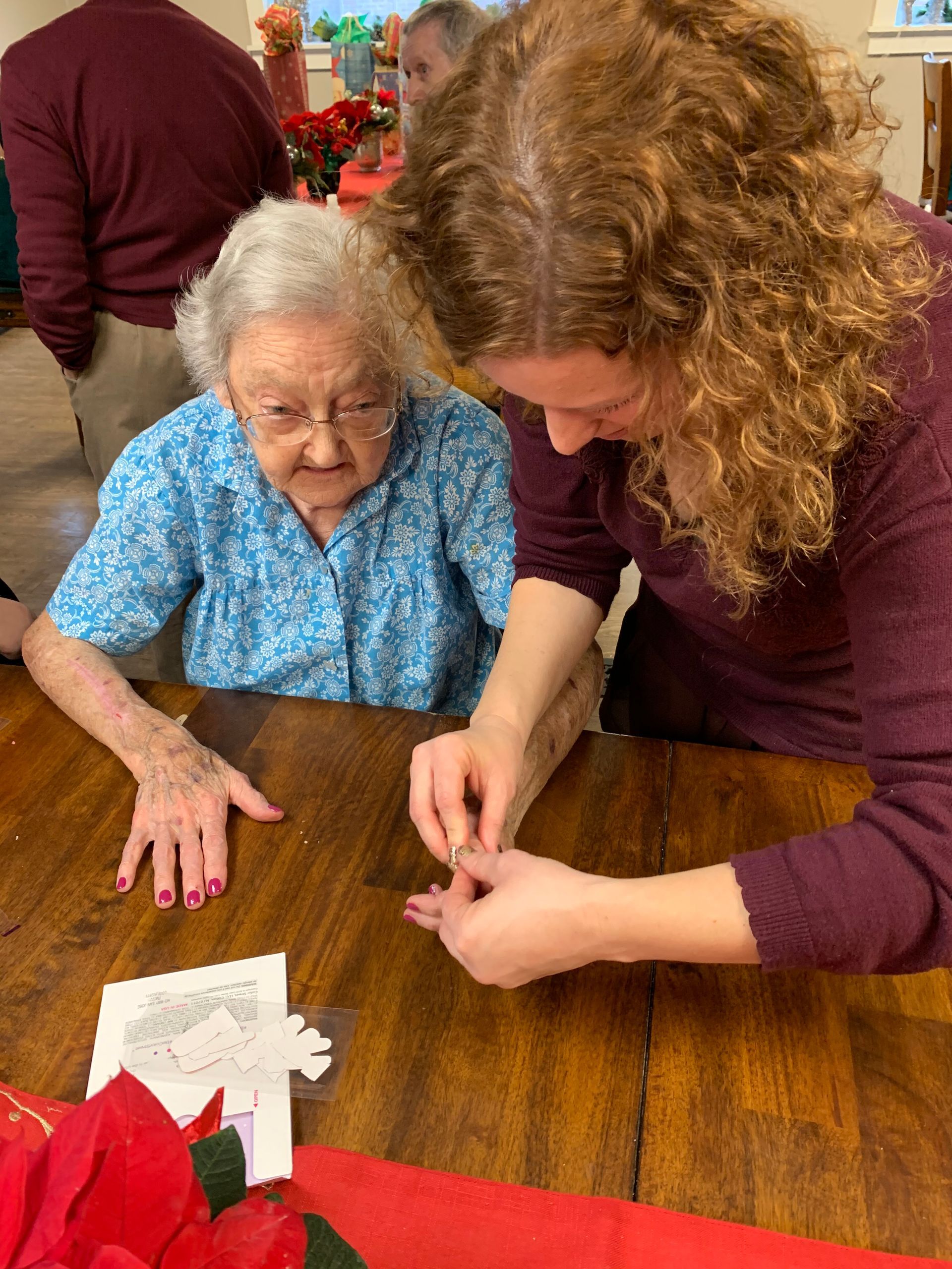 A woman is helping an older woman make a paper snowflake.