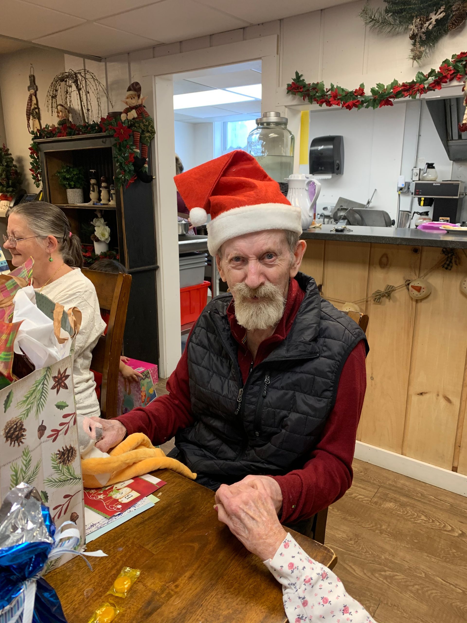 An elderly man wearing a santa hat is sitting at a table.