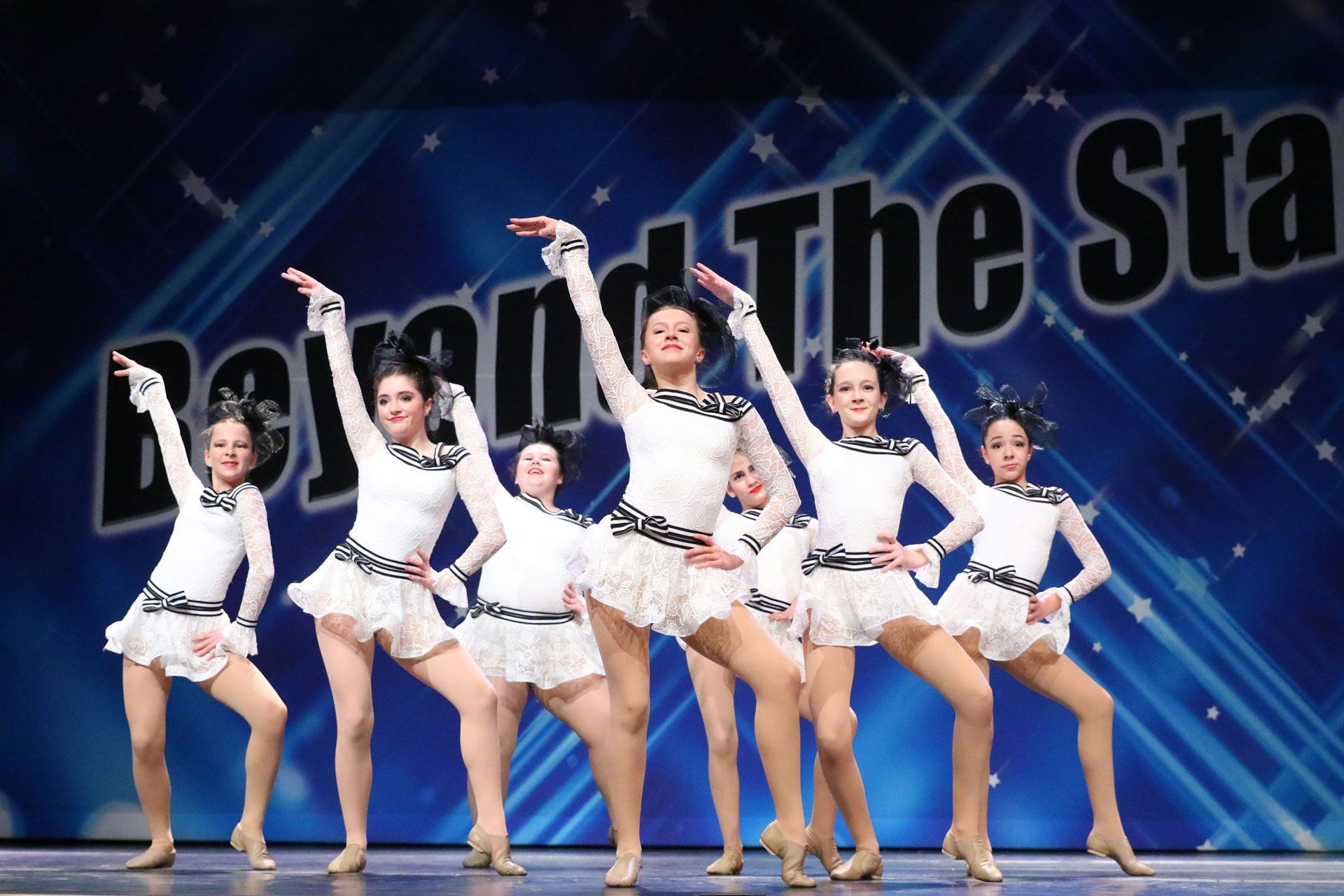A group of young girls are dancing in front of a sign that says beyond the stars