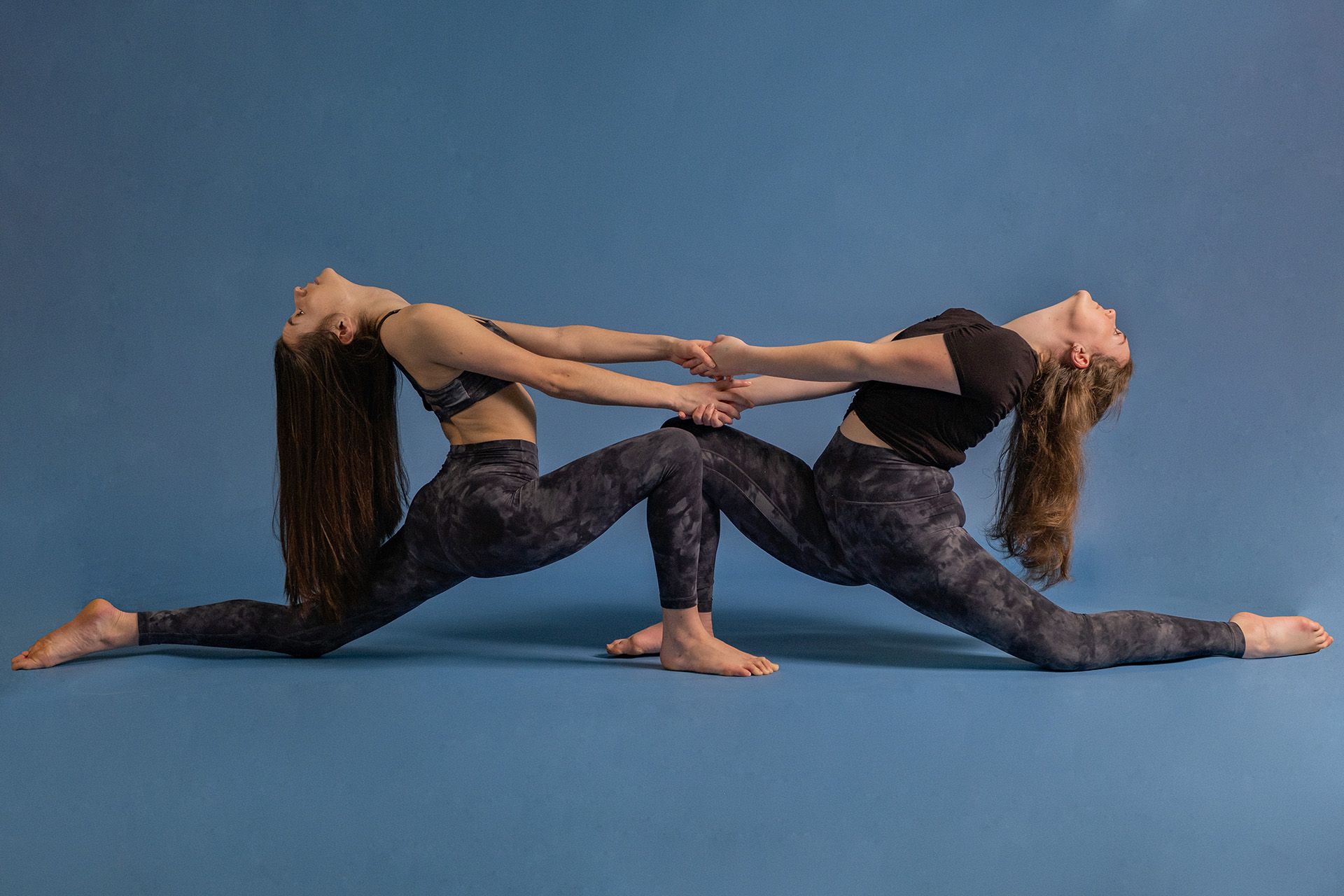Two women are doing yoga together on a blue background.