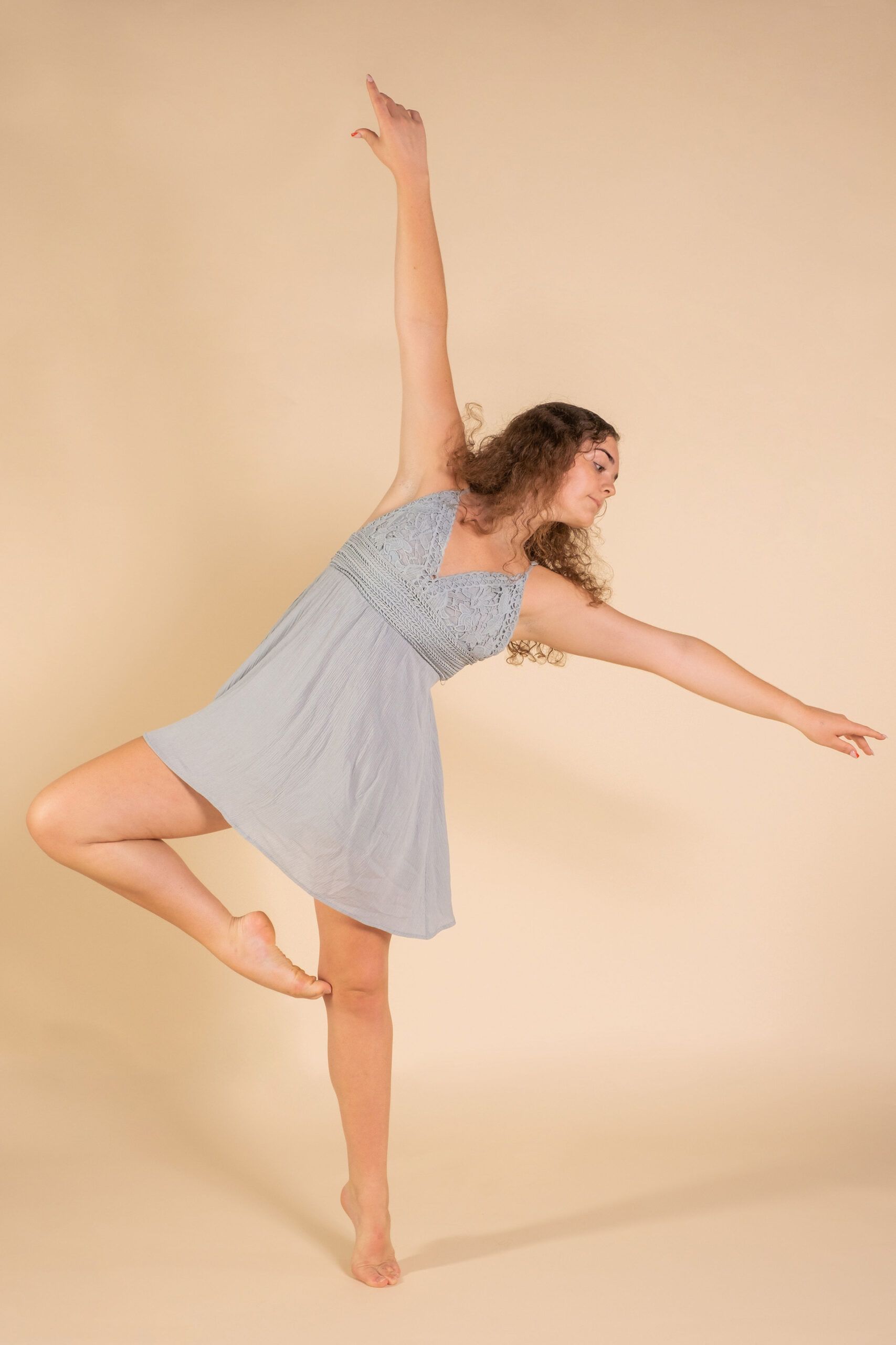 A woman in a blue dress is dancing on one leg.