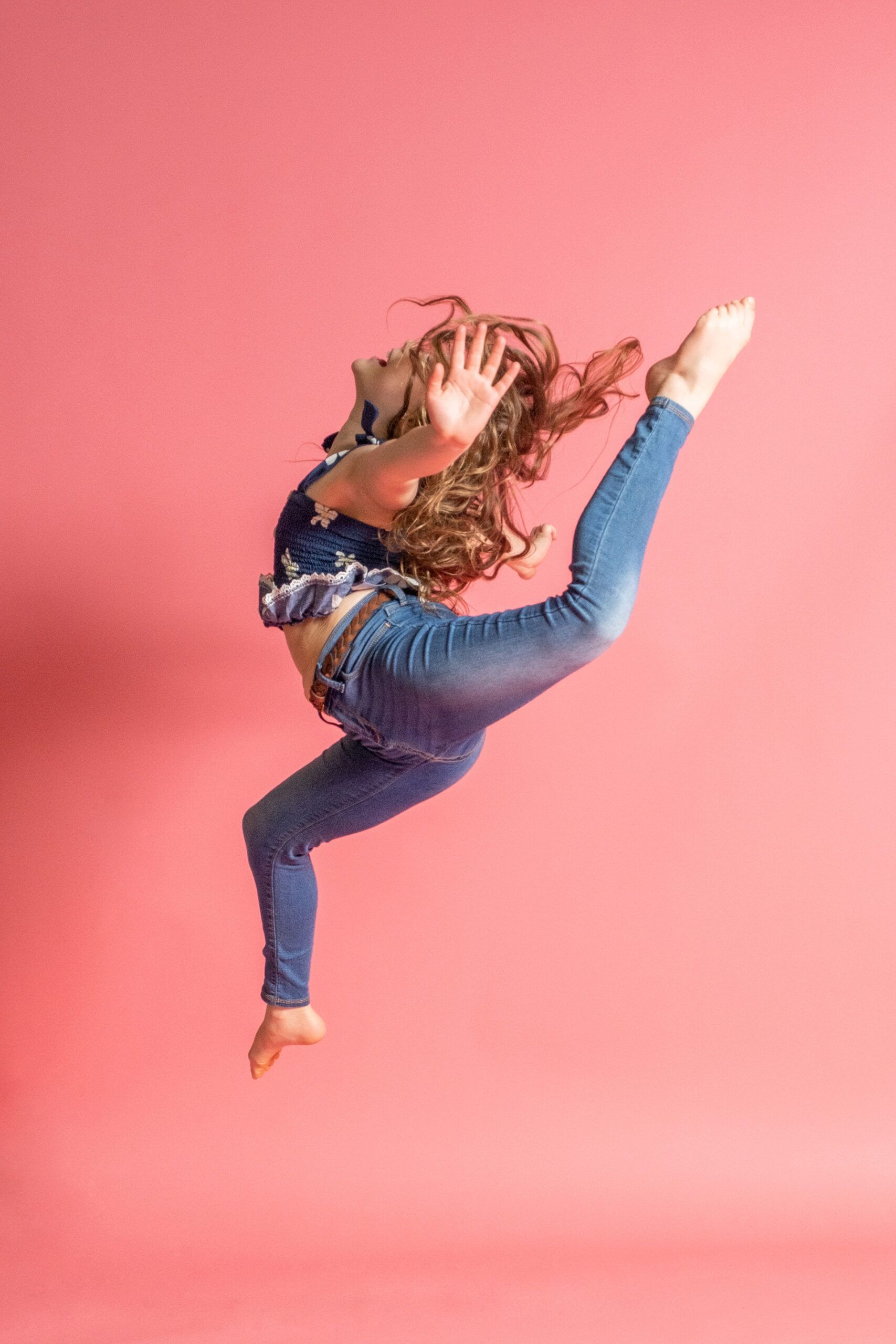 A young girl is jumping in the air on a pink background.
