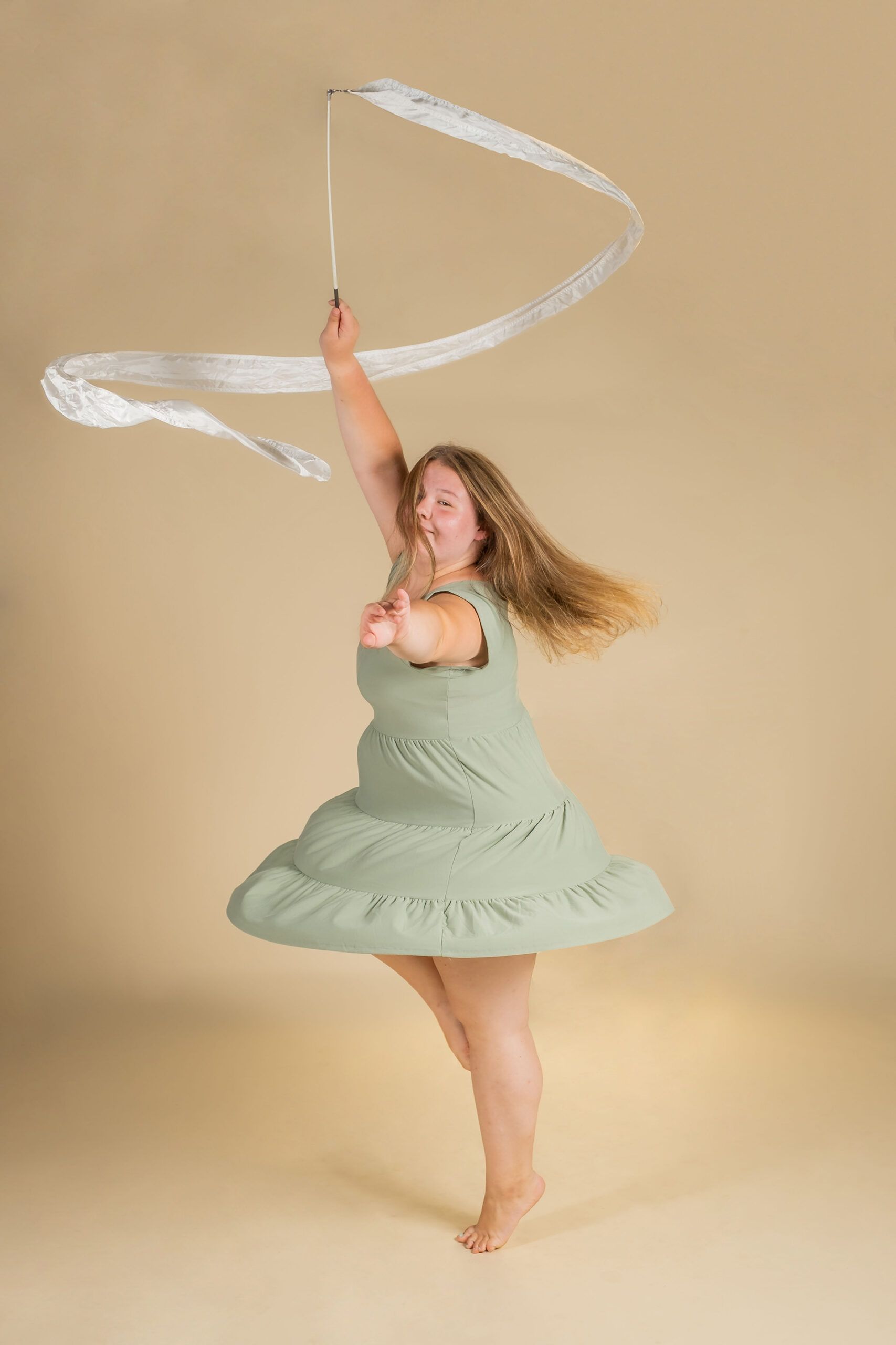 A woman in a green dress is dancing with a white ribbon.