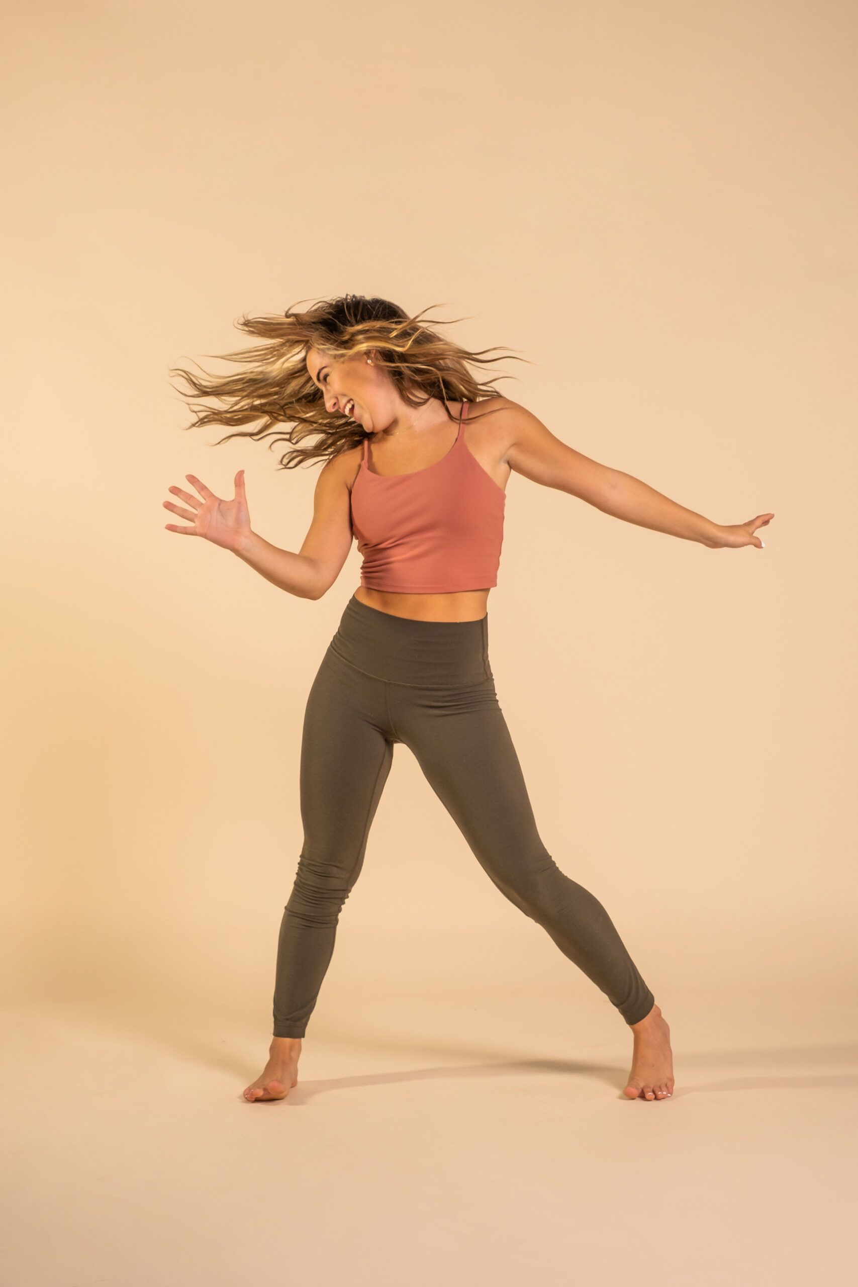 A woman in a pink tank top and green leggings is dancing.