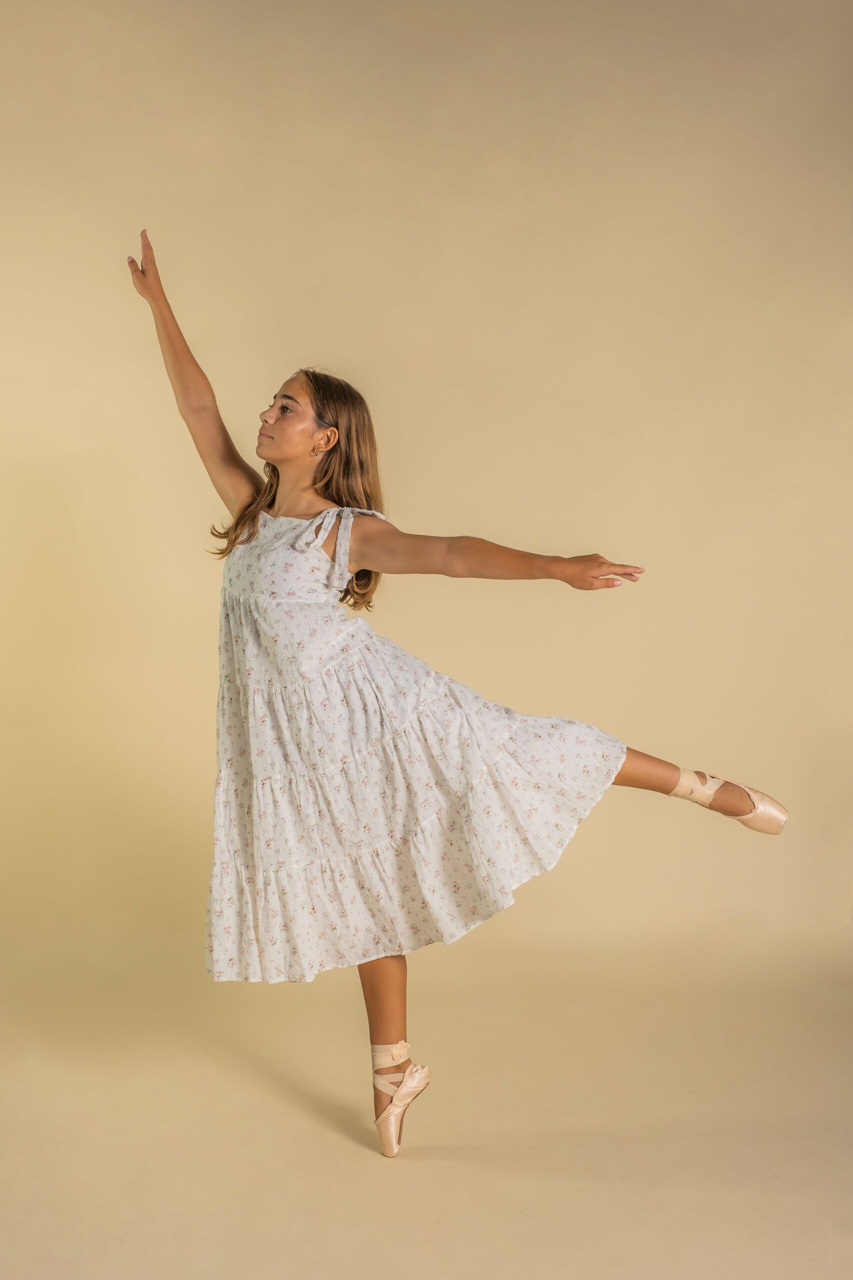 A young girl in a white dress and pointe shoes is dancing.