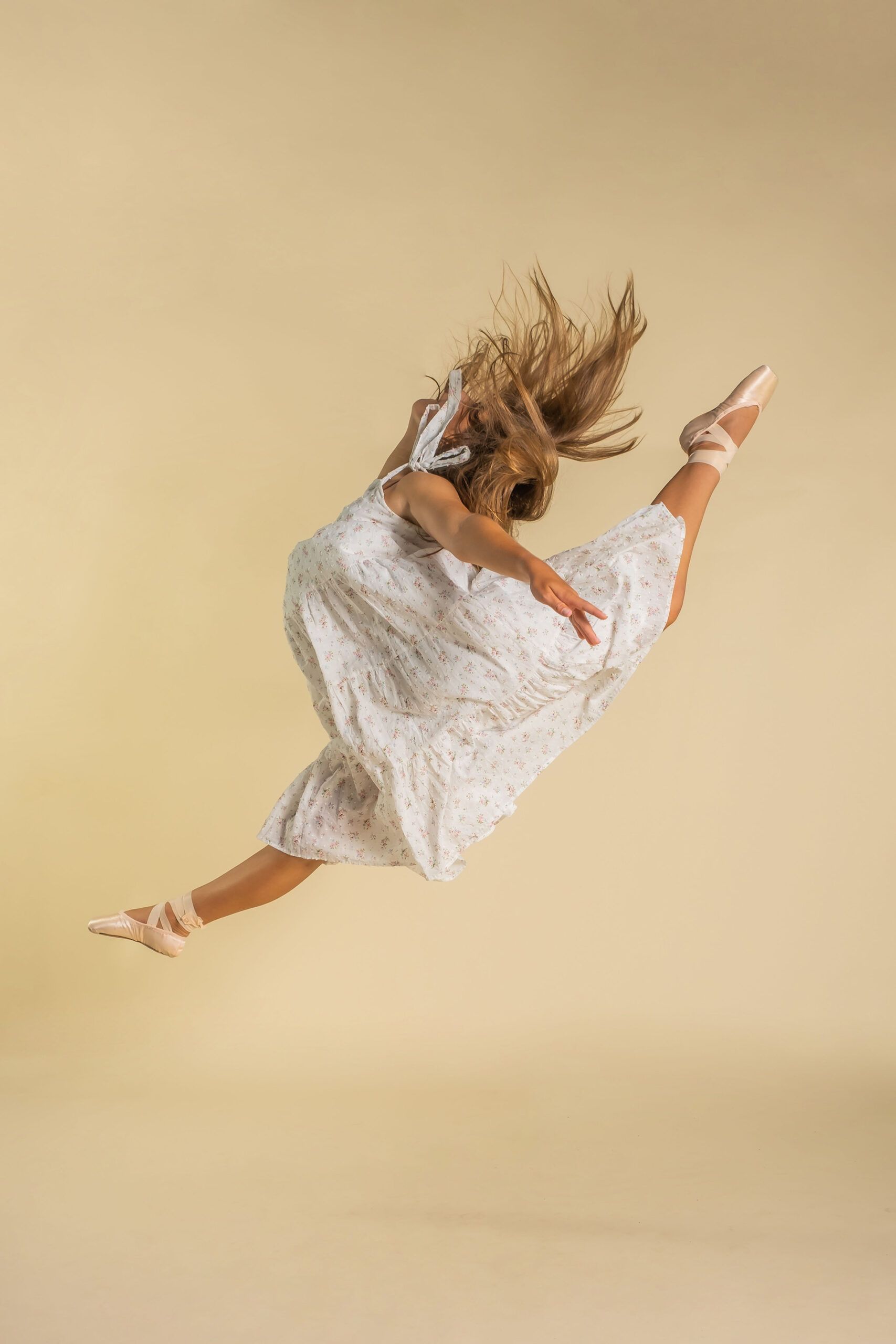 A woman in a white dress and pointe shoes is jumping in the air.