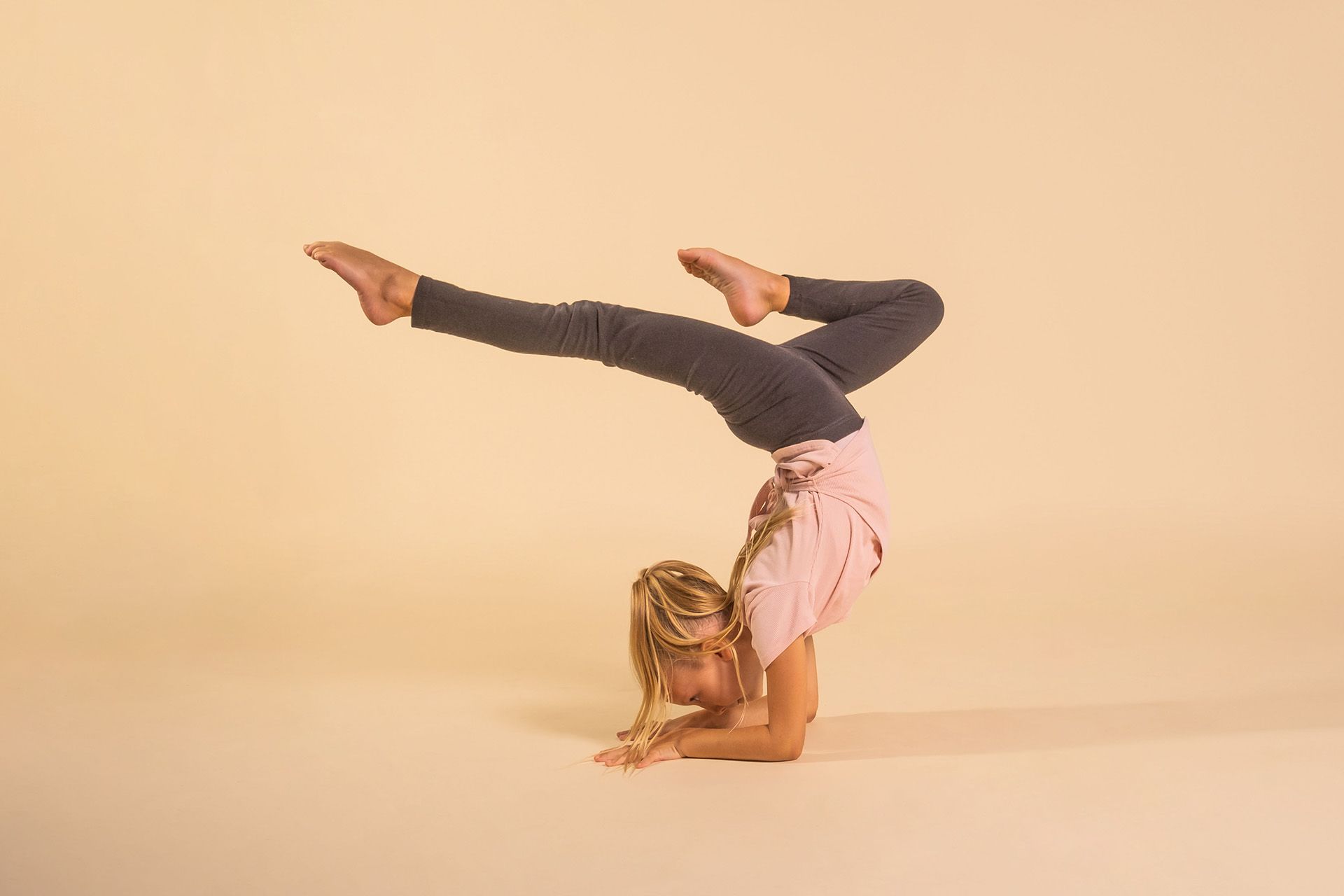 A young girl is doing a handstand on a beige background.