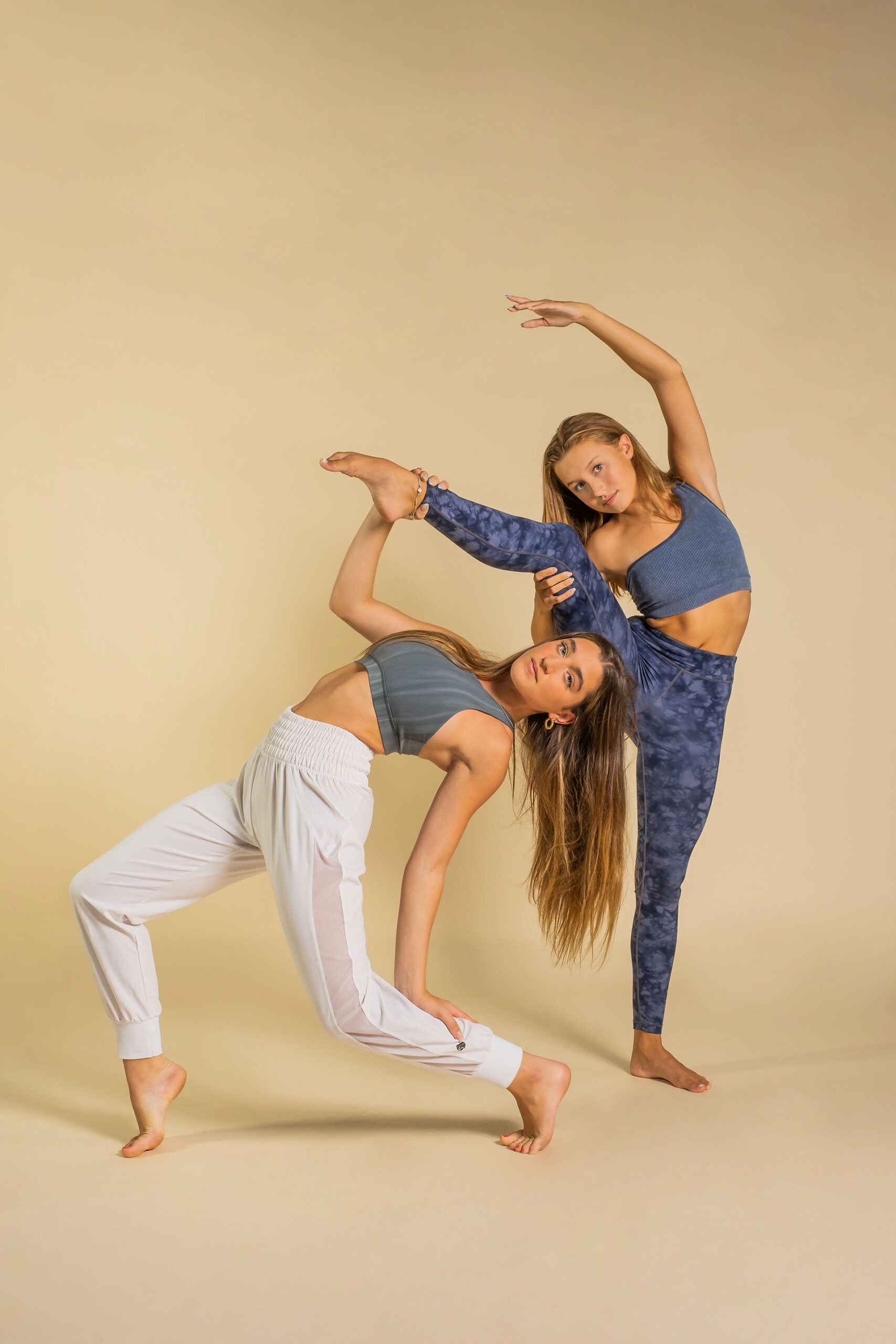 Two young women are doing yoga poses together on a beige background.
