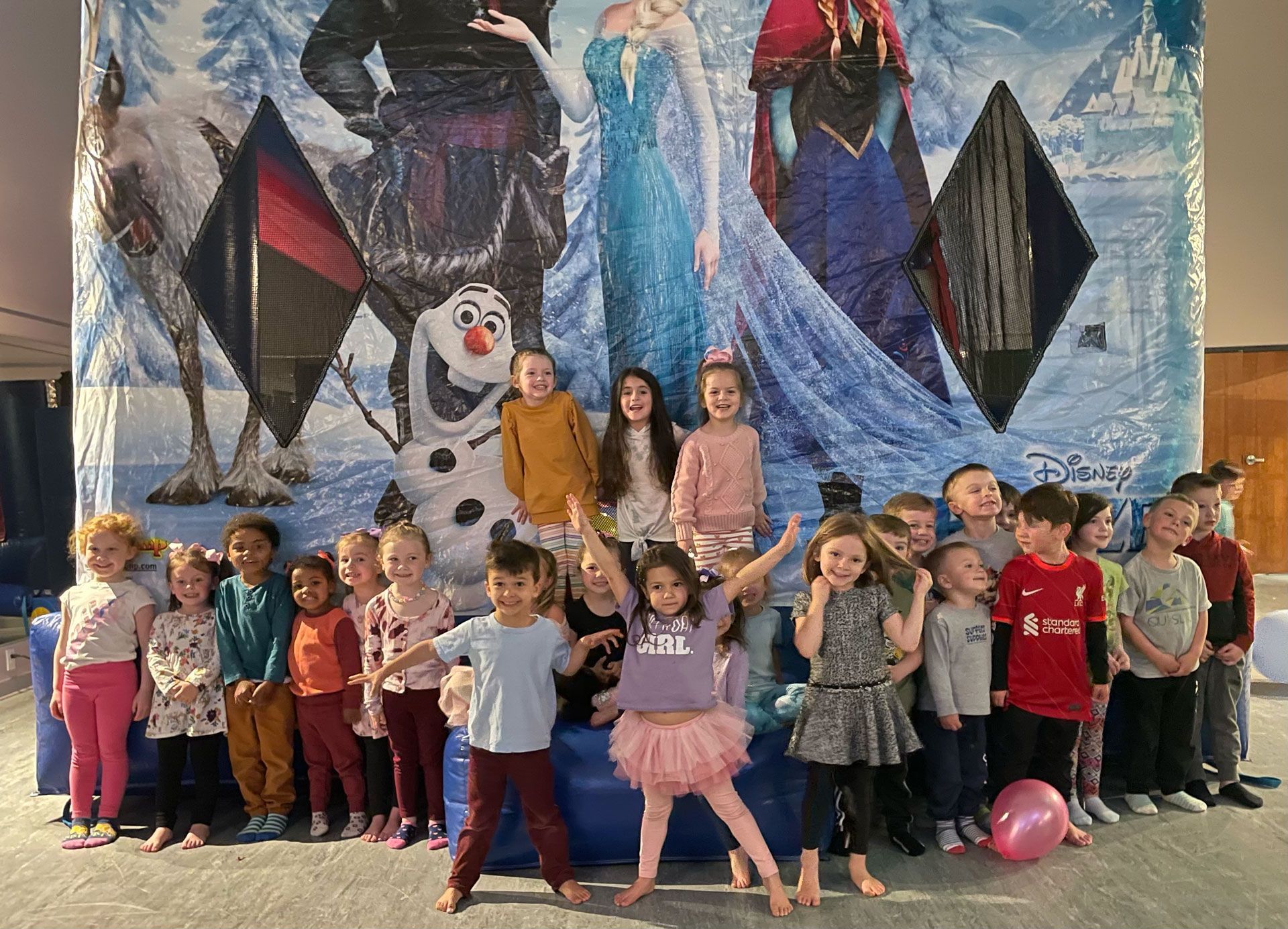 A group of children are posing for a picture in front of a frozen poster.