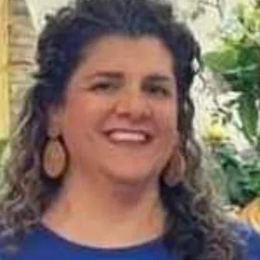A woman wearing a blue shirt and earrings is smiling for the camera.