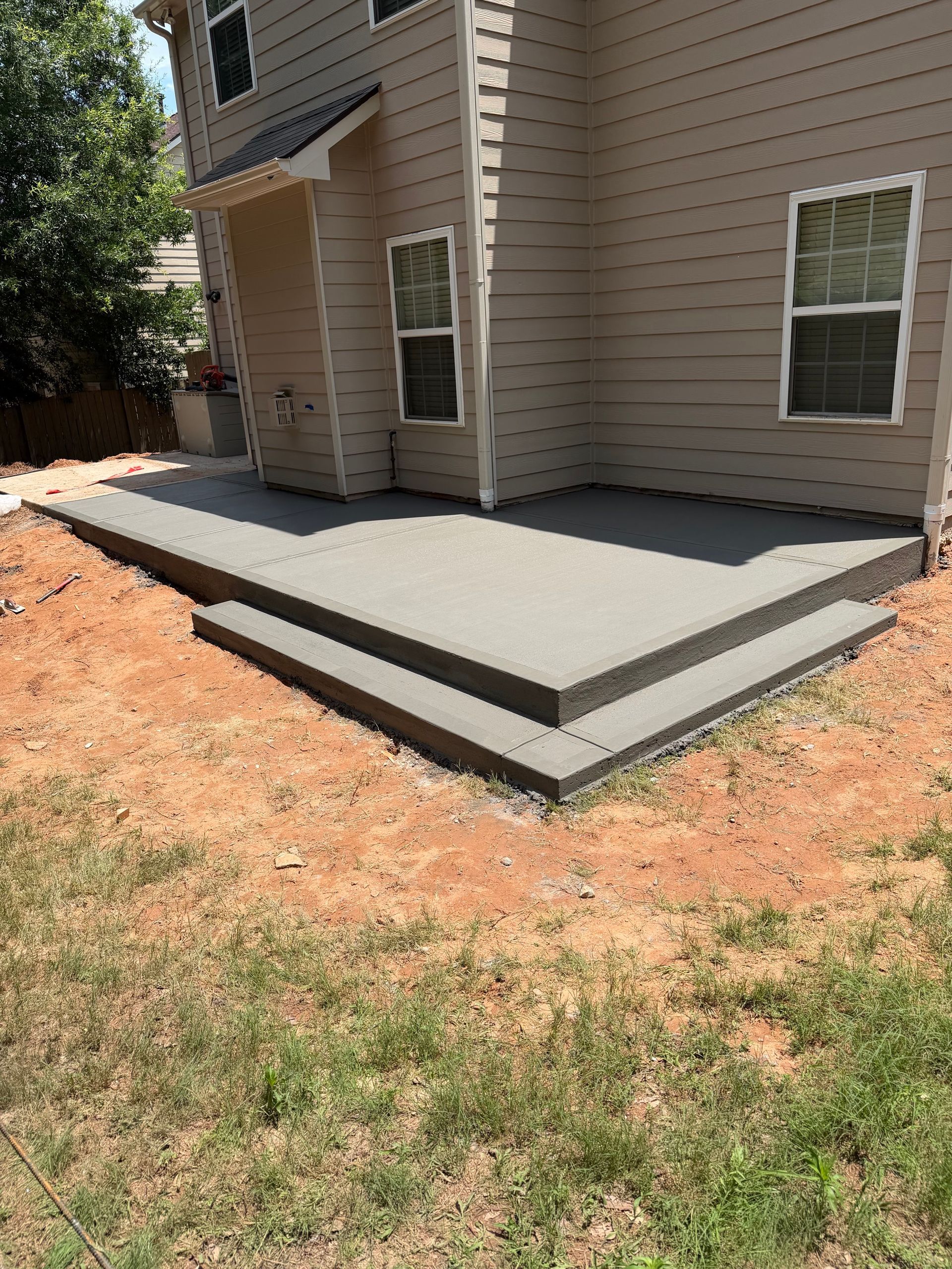 Concrete patio beside beige house with white trim and a small front step.