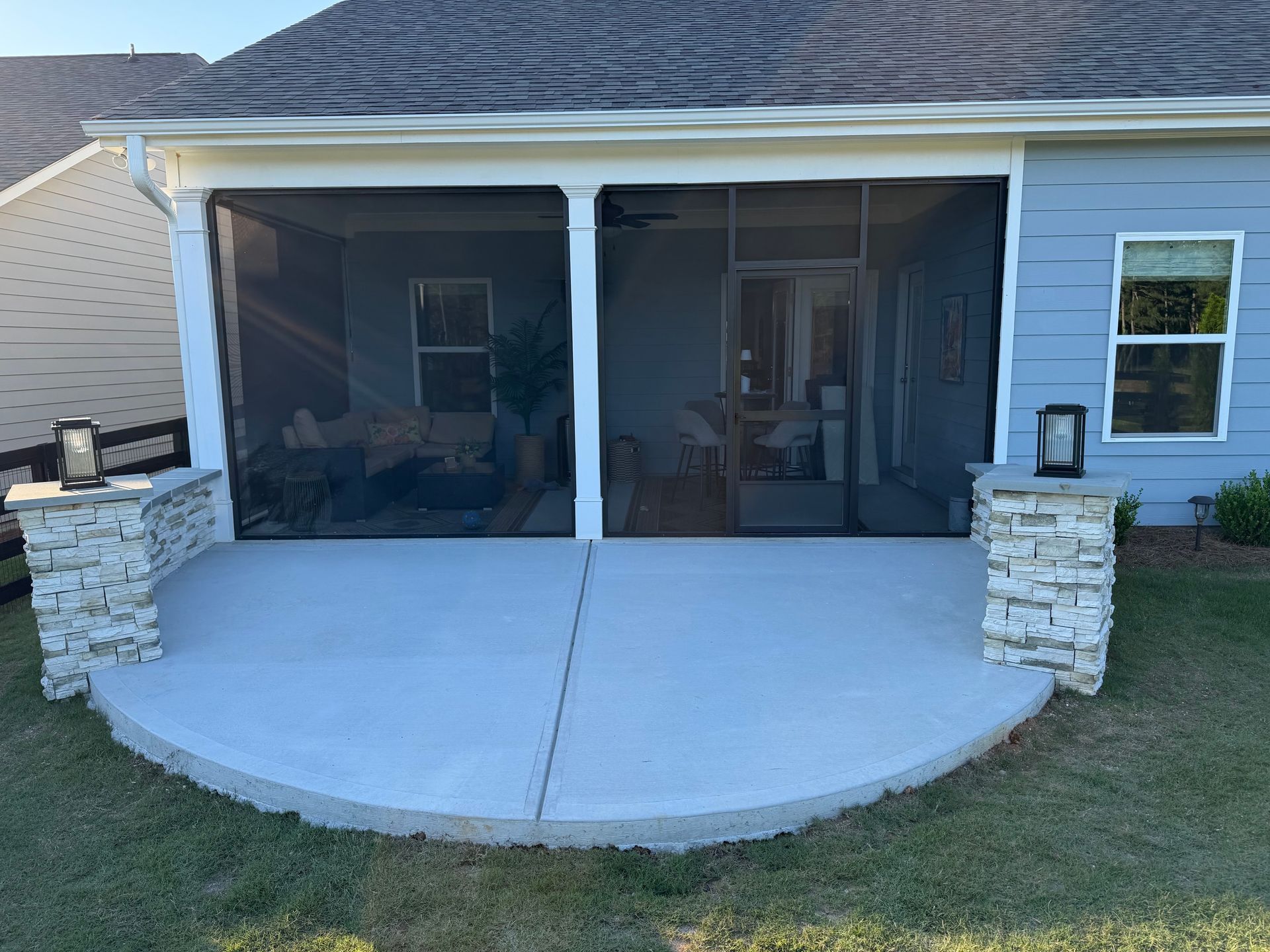 Screened-in front porch with white columns, stone half walls, and a curved concrete patio.