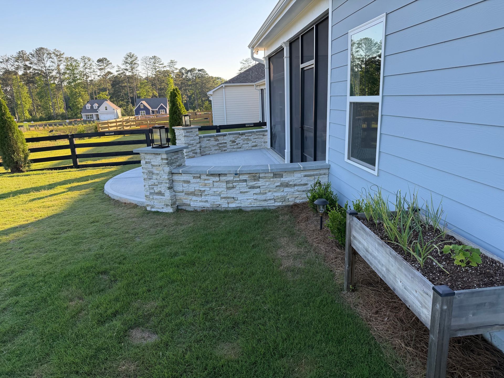 Backyard patio with stone steps beside a gray house and raised garden bed by a grassy lawn