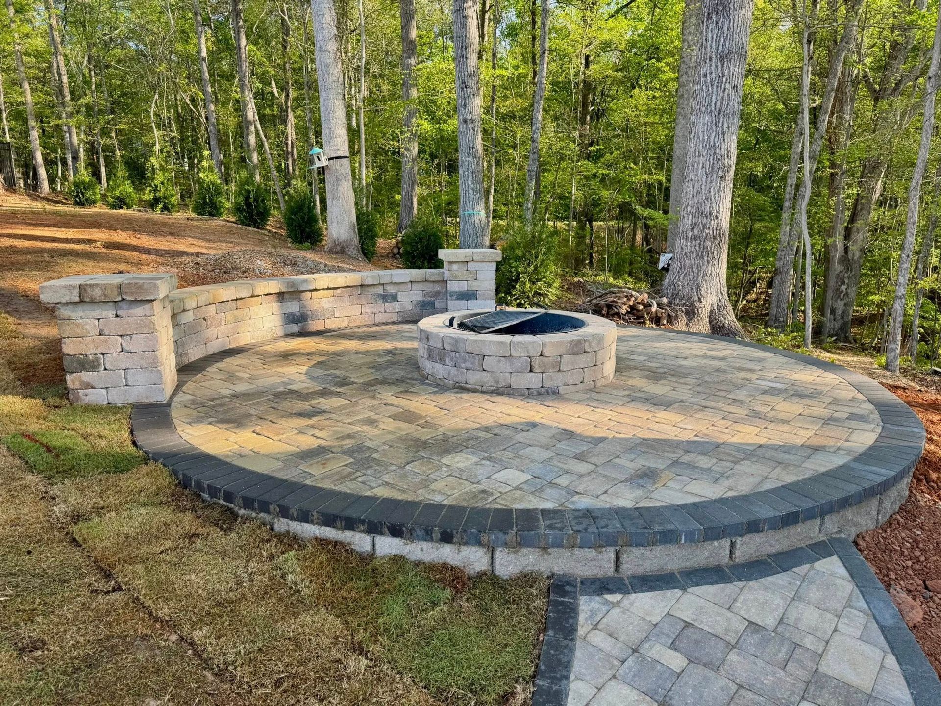 Circular paved patio with a fire pit and low seating, surrounded by trees.