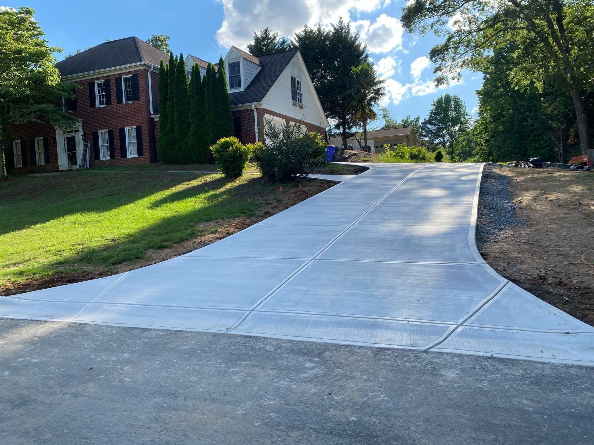 Concrete driveway leads to a two-story house with green lawn and trees.