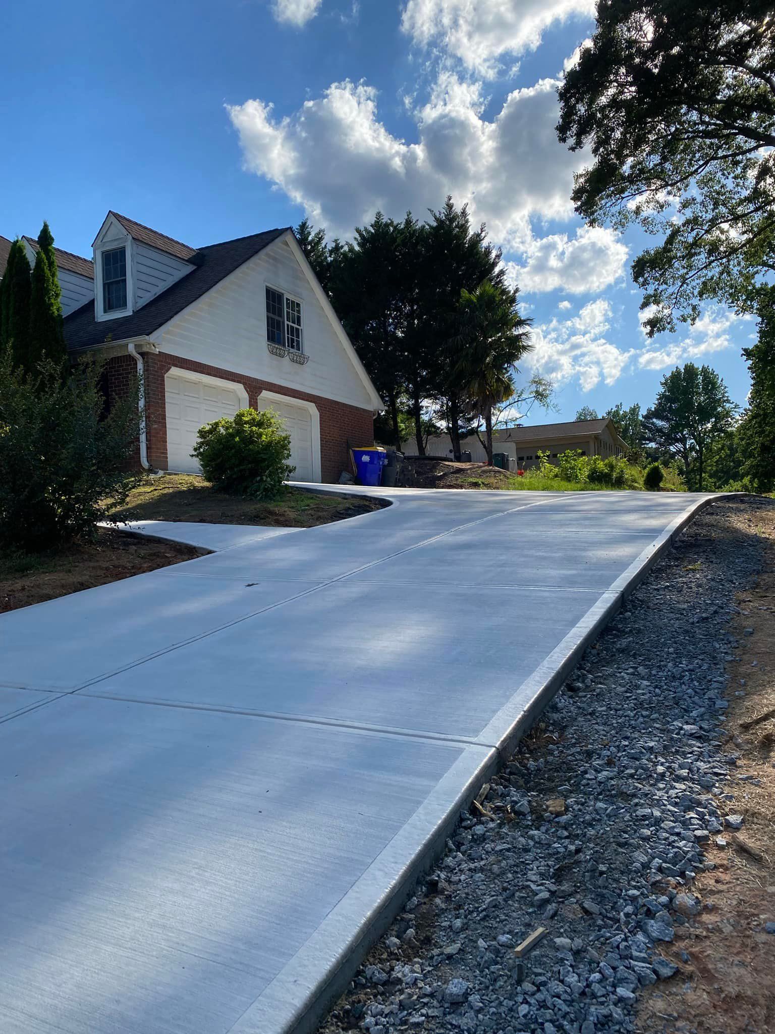 Newly poured concrete driveway leading to a two-story house with a blue sky and fluffy clouds.