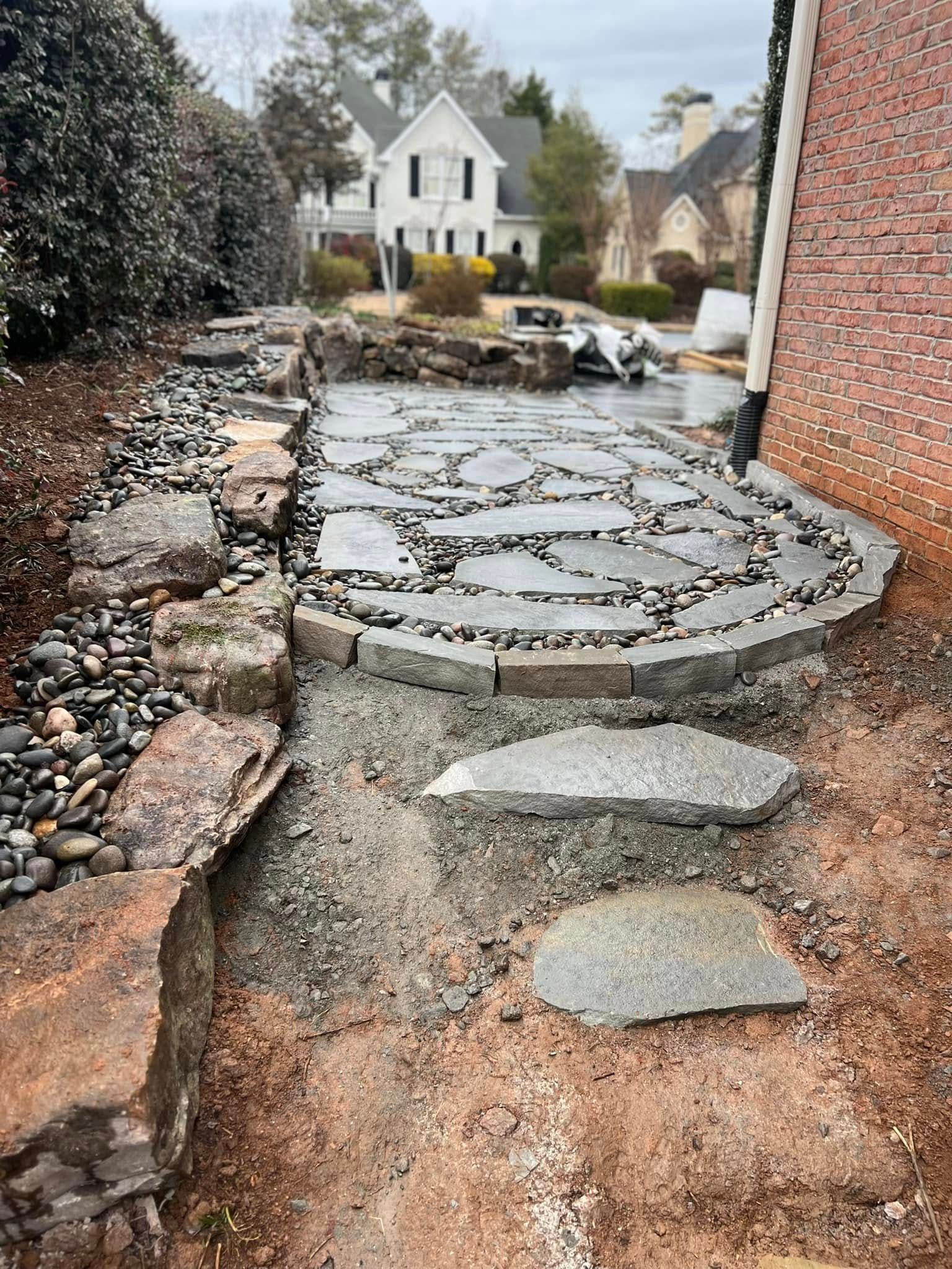 Stone patio with stepping stones and landscaping. Grey cobblestone path leads to brick building.