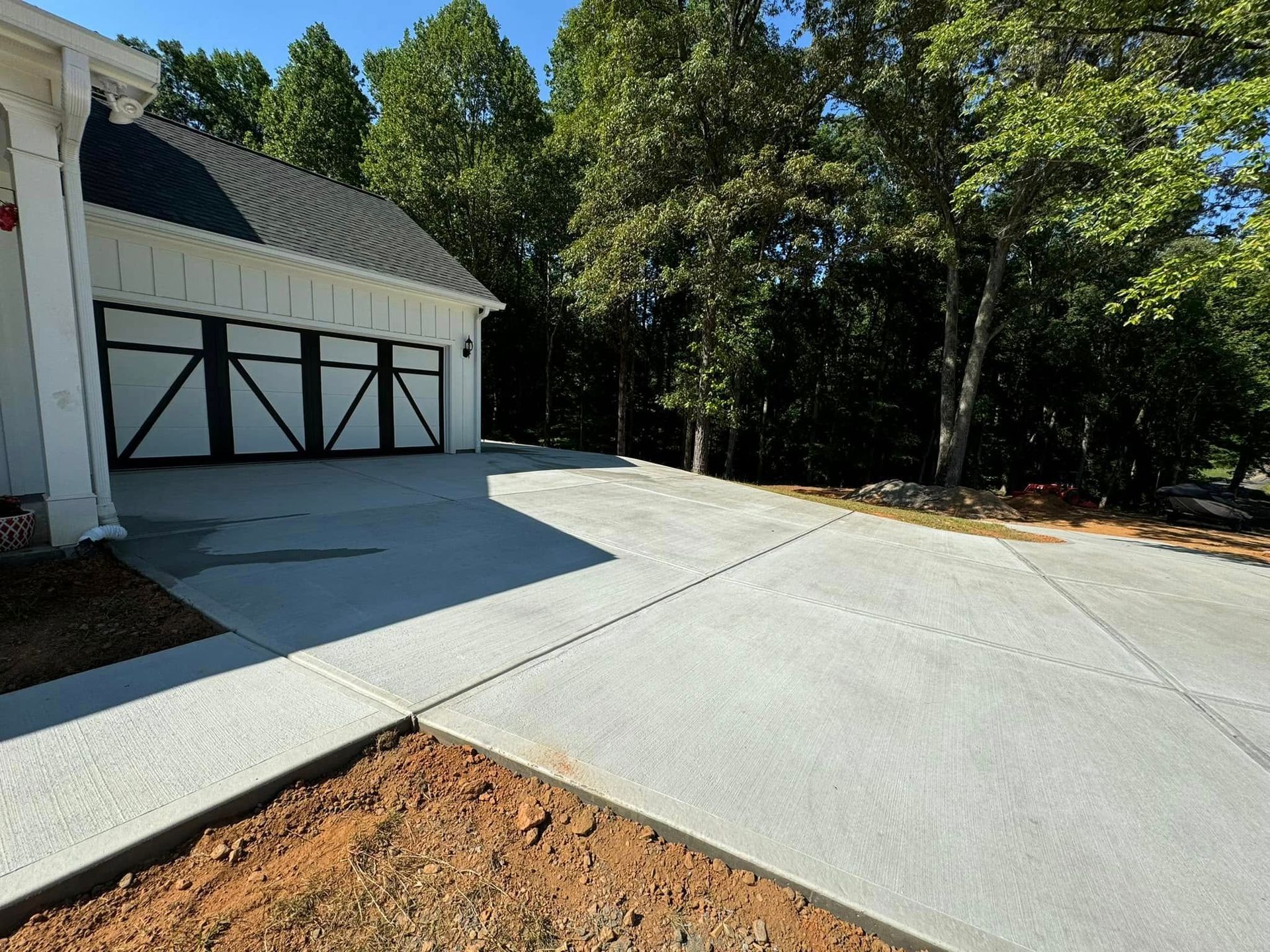 Driveway in front of a white garage with black doors; trees in the background, blue sky.