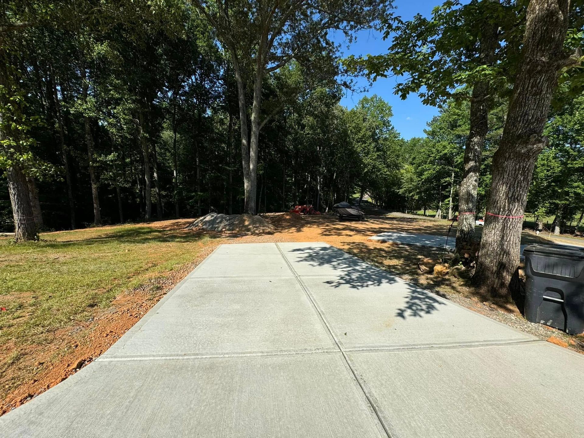 Concrete driveway leading towards trees on a sunny day.
