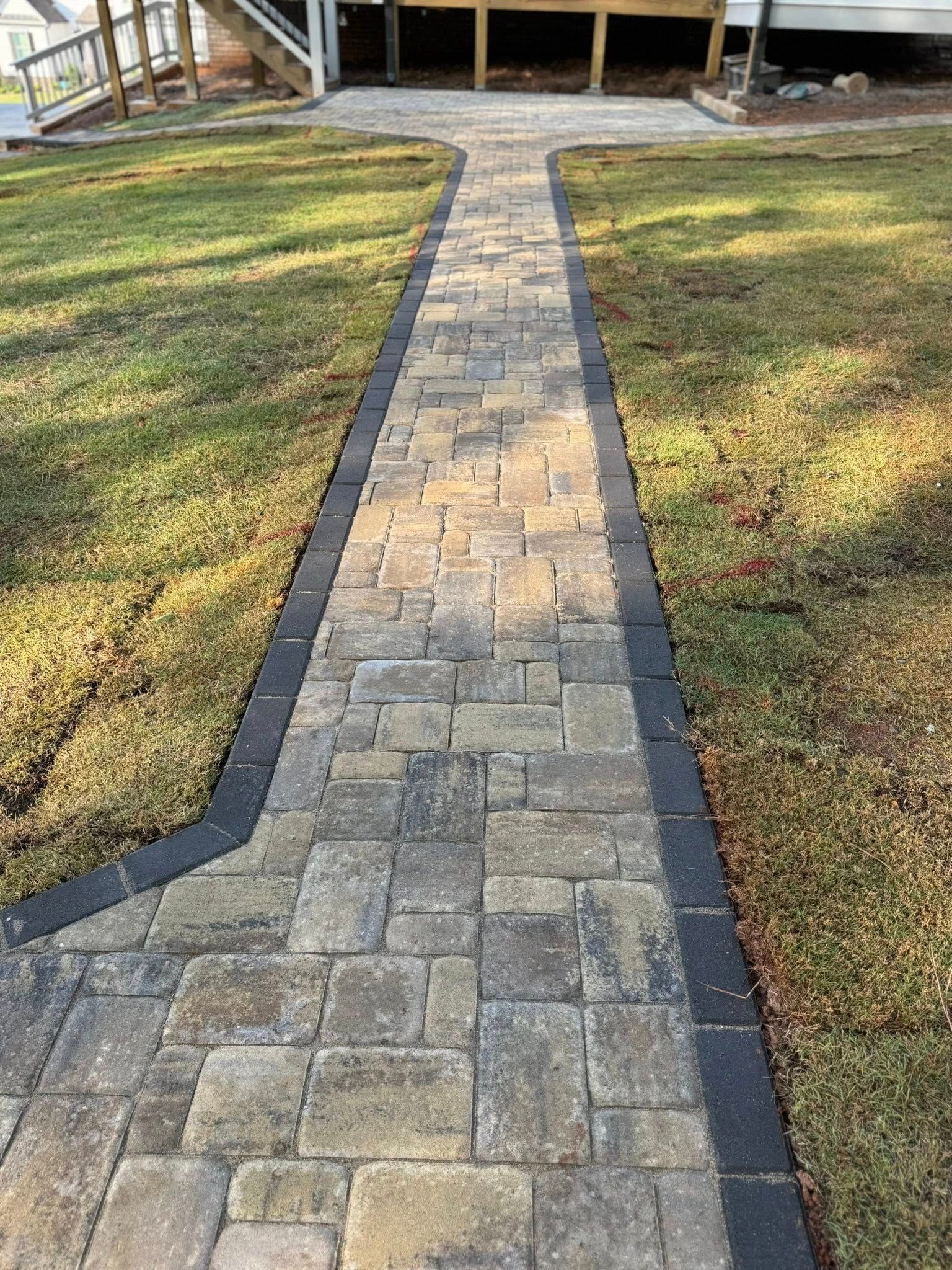 Stone pathway leads from grass to a raised wooden deck; dark edging borders the path.