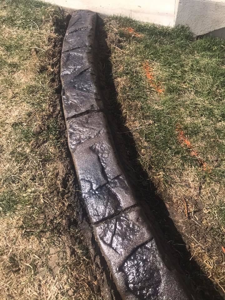 Stone-patterned concrete curbing borders a lawn, dark grey with a curved shape.