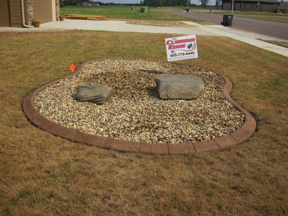 Landscaped rock garden with stone border and two large rocks in front yard.