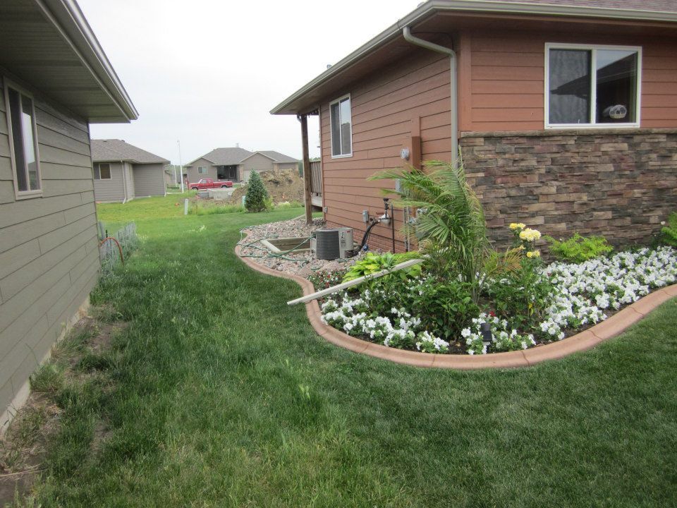 Houses with grassy yards, one with a brown stone flowerbed border filled with flowers.