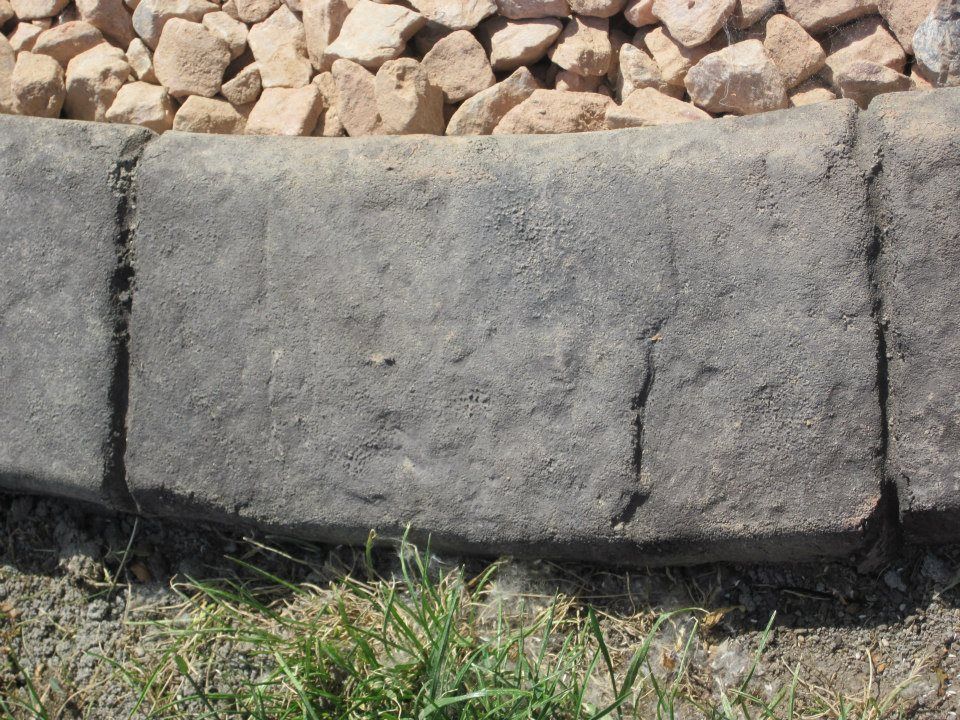 Gray stone curbing separating tan gravel from green grass.