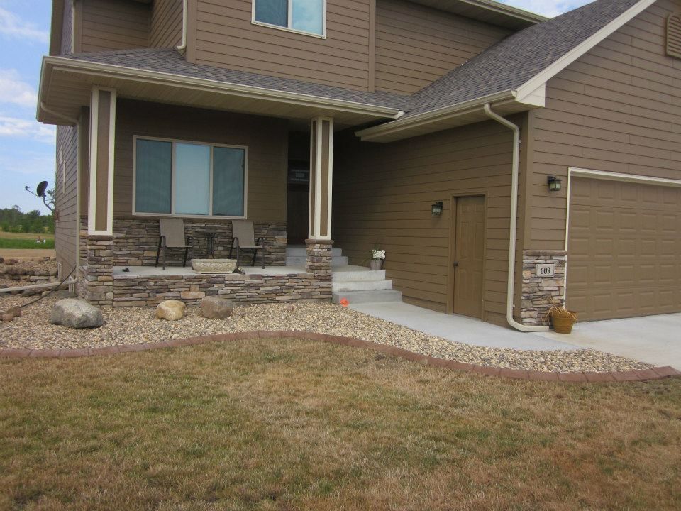 Brown house with tan trim, a porch, and a garage; a stone-edged walkway leads to the front door.
