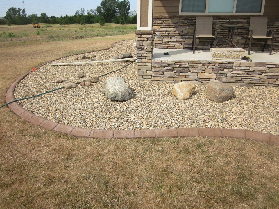 Stone landscaping around a house foundation, with a brown border and three large rocks.