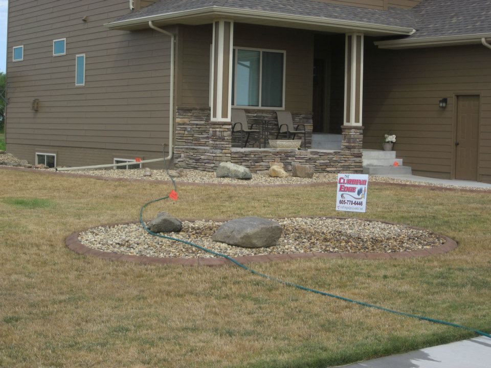 House with rock landscaping and brown siding. A sign is in the yard.