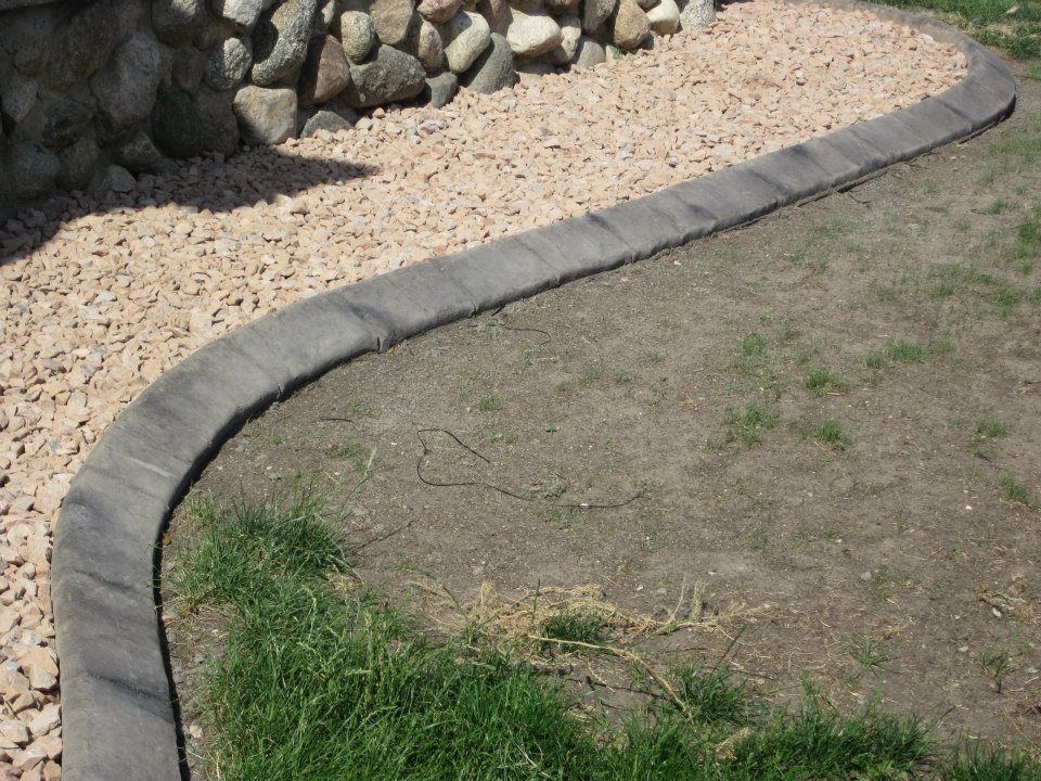 Curved concrete curbing separates gravel and grass near a stone wall.