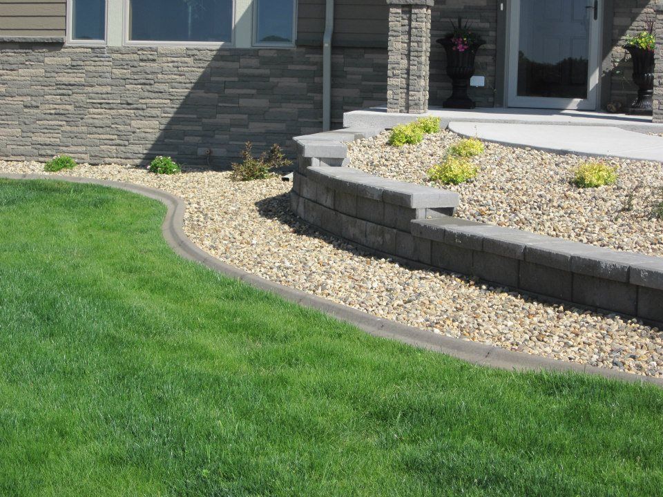 Green lawn curving into a tan gravel bed, next to a retaining wall and house exterior.
