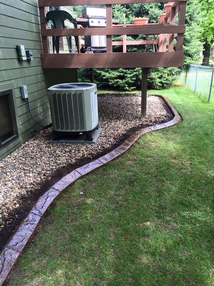 Air conditioner unit next to a house with a raised wooden deck, surrounded by decorative border and grass.