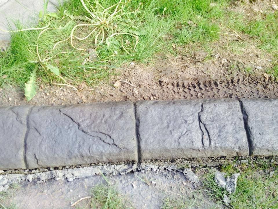 Gray concrete border separating grass and dirt with weeds.