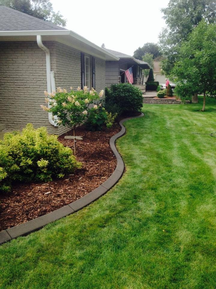 A house with green grass and a flower bed edged with dark border and mulch.