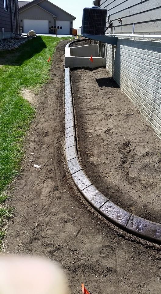 Curved, brown concrete edging along a house foundation, separating soil from grass.