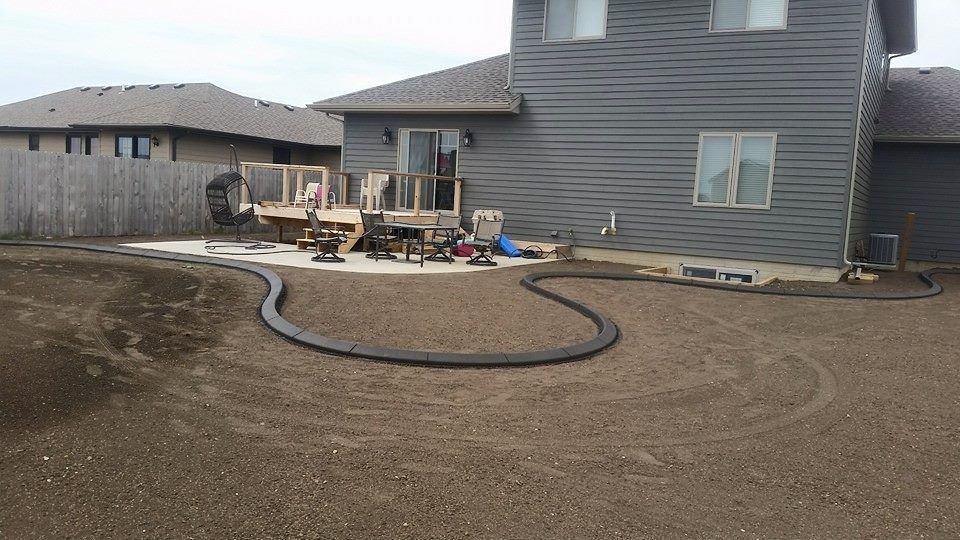 Backyard with concrete patio, landscaping border, house, and deck.