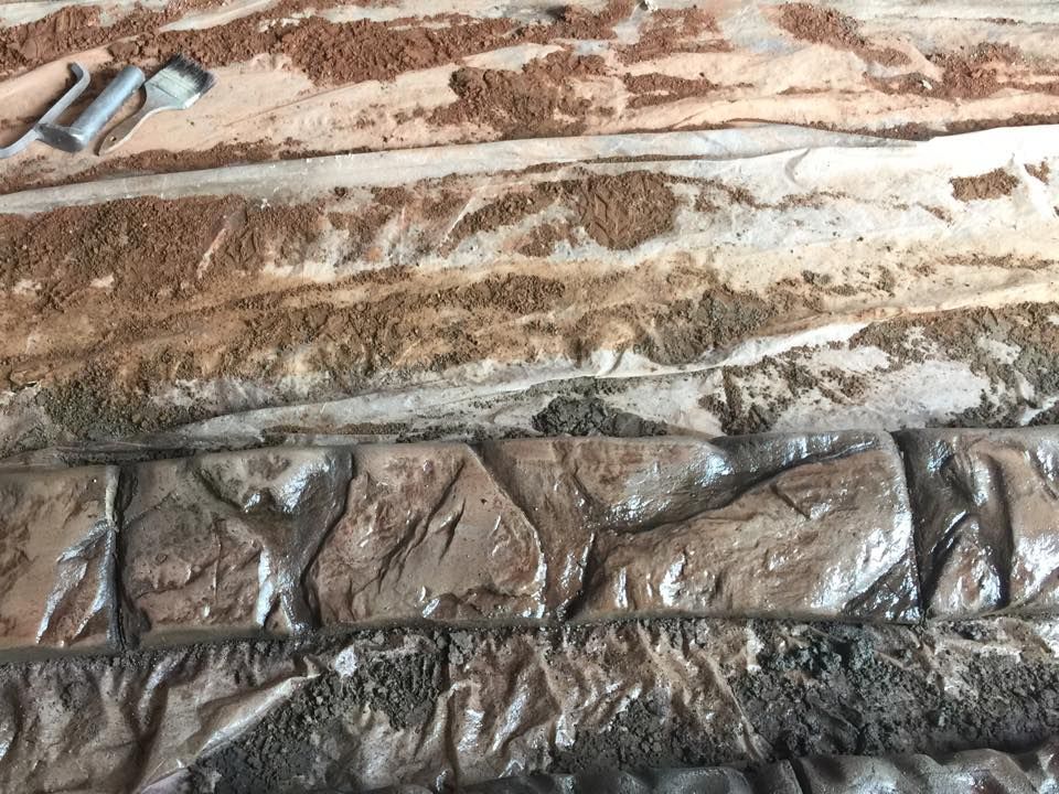 Stamped concrete, textured to resemble stone, is being worked on with tools, showing layers of color.