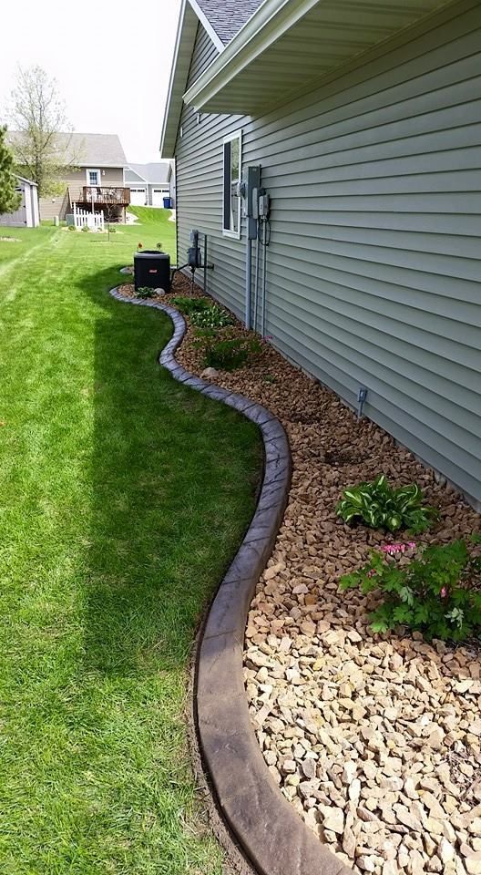 A house with gray siding and a curved, concrete landscape border along a bed of mulch and plants.