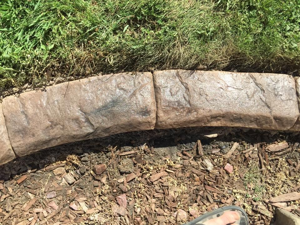 Brown, textured concrete curbing bordering a bed of mulch and green grass.