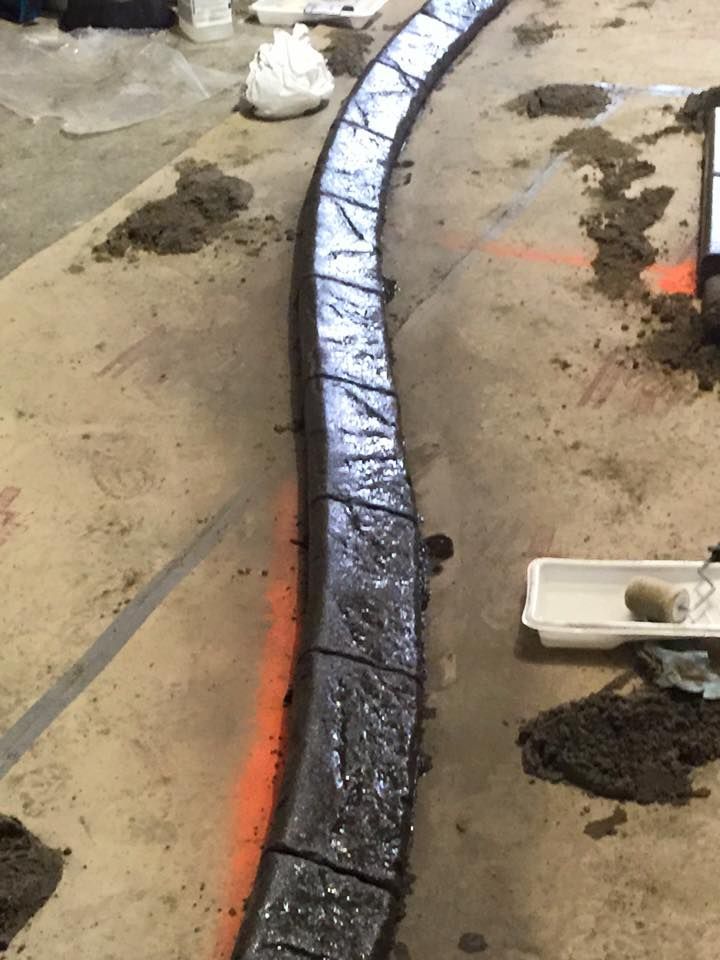 A dark, textured concrete curb runs along a dirt area, possibly a landscaping project.