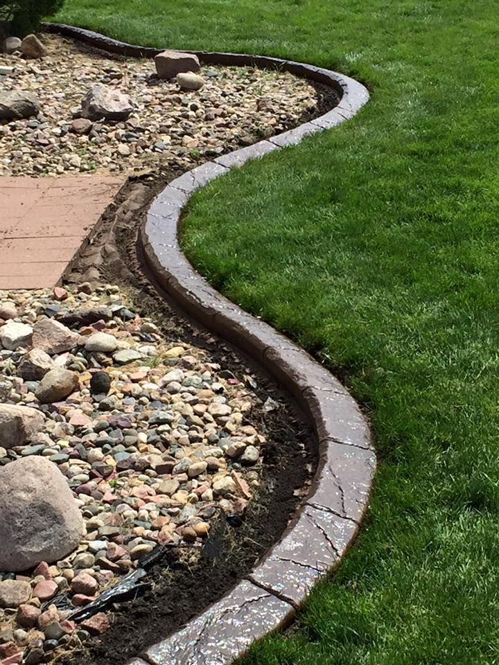 Curved concrete landscape edging separating green grass from a bed of rocks.