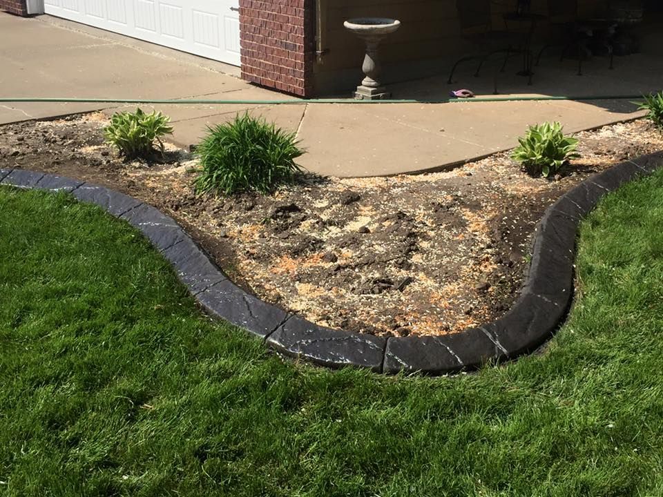 Black concrete landscape edging defines a flowerbed in a grassy yard.