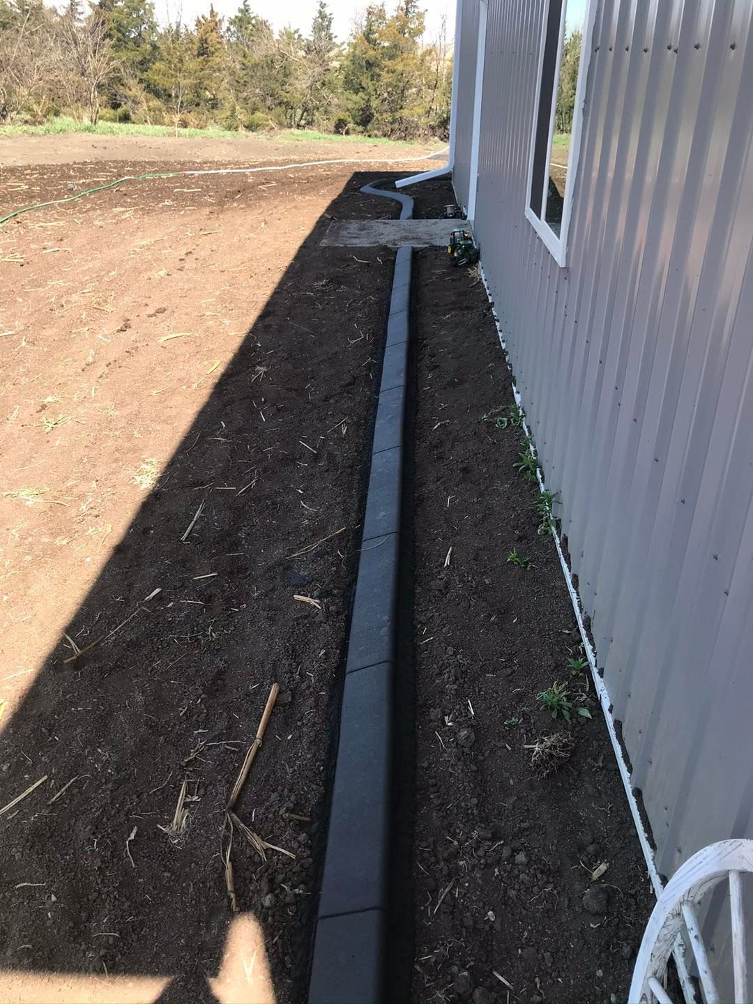 Black edging borders a strip of dark soil along a gray building.