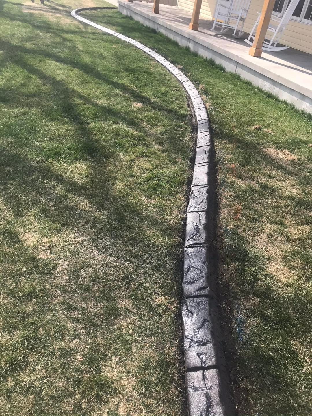 Curved dark gray concrete edging along green grass next to a house.