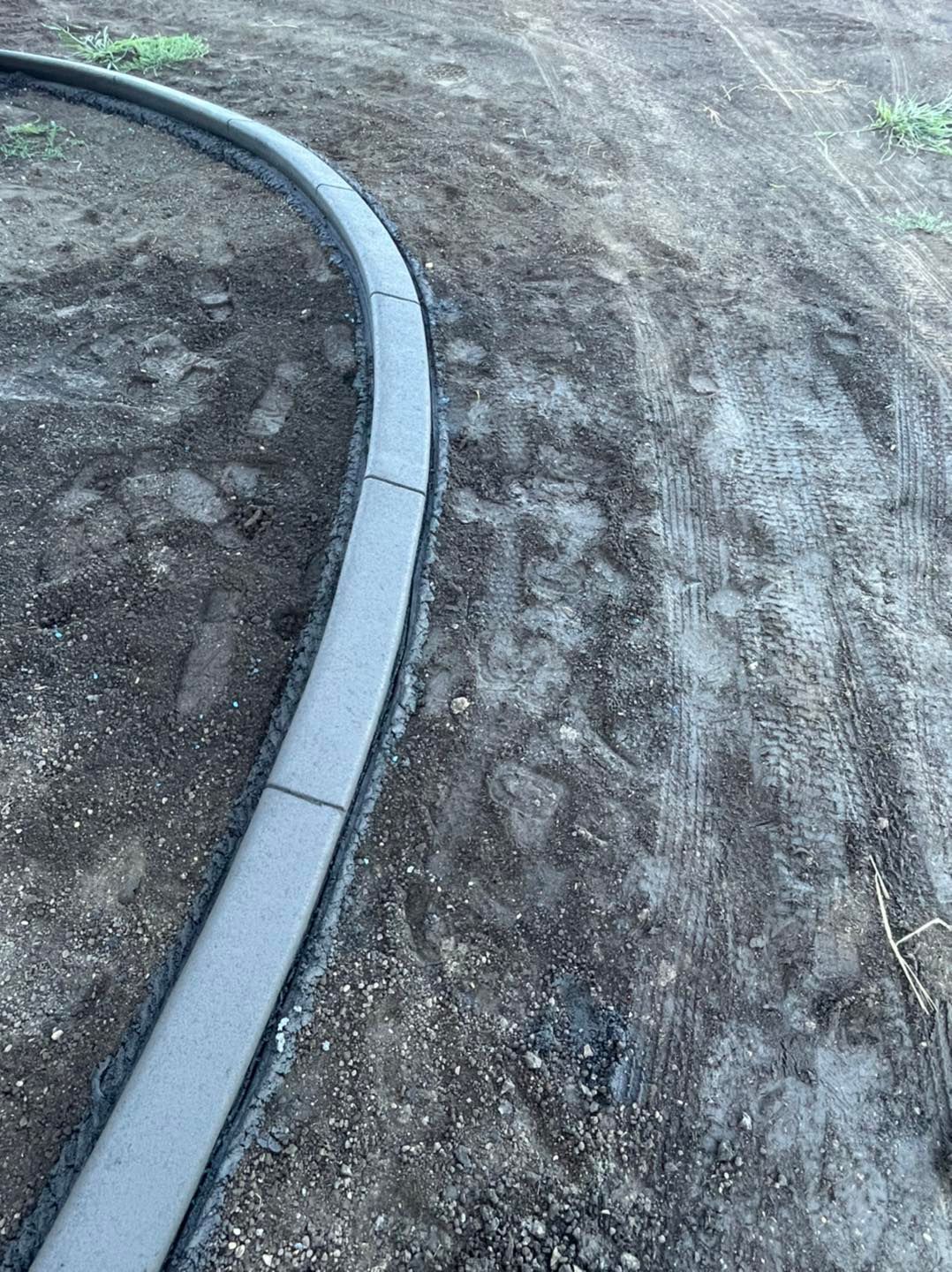 Curved concrete curb edging a dirt area.