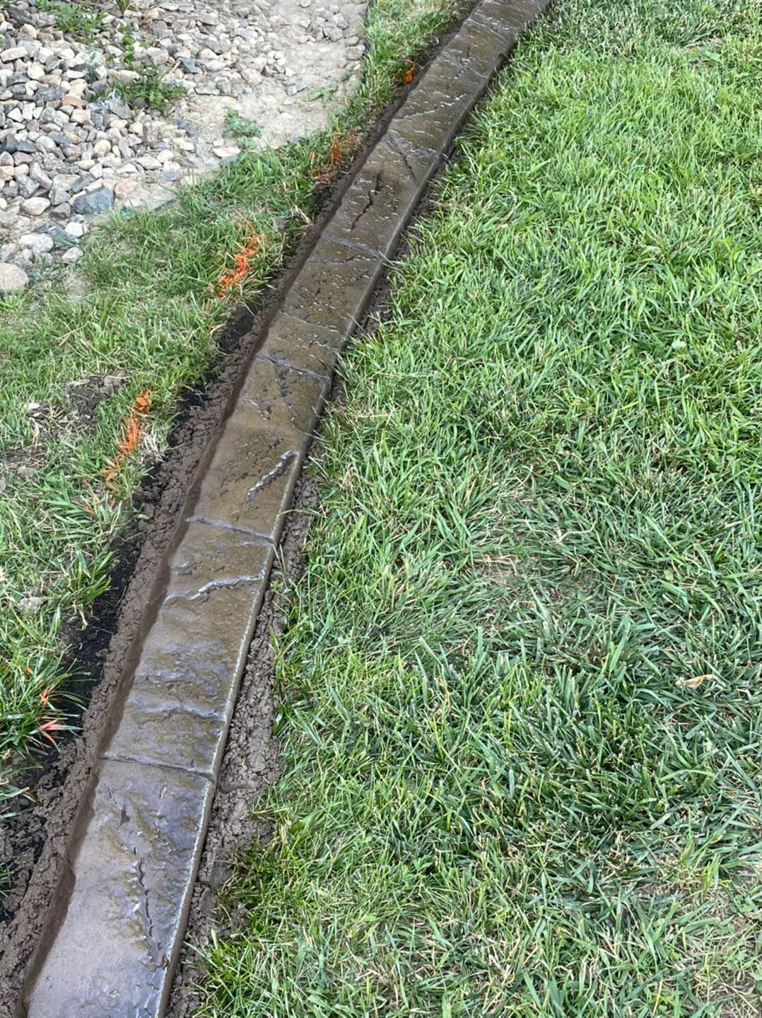 A curved, stamped concrete landscape border separates a patch of gravel from a manicured grass lawn.