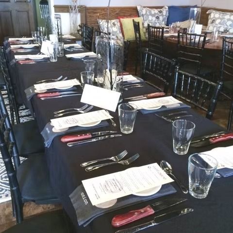 Set dining tables with black tablecloths, menus, glasses, and chairs in a restaurant.